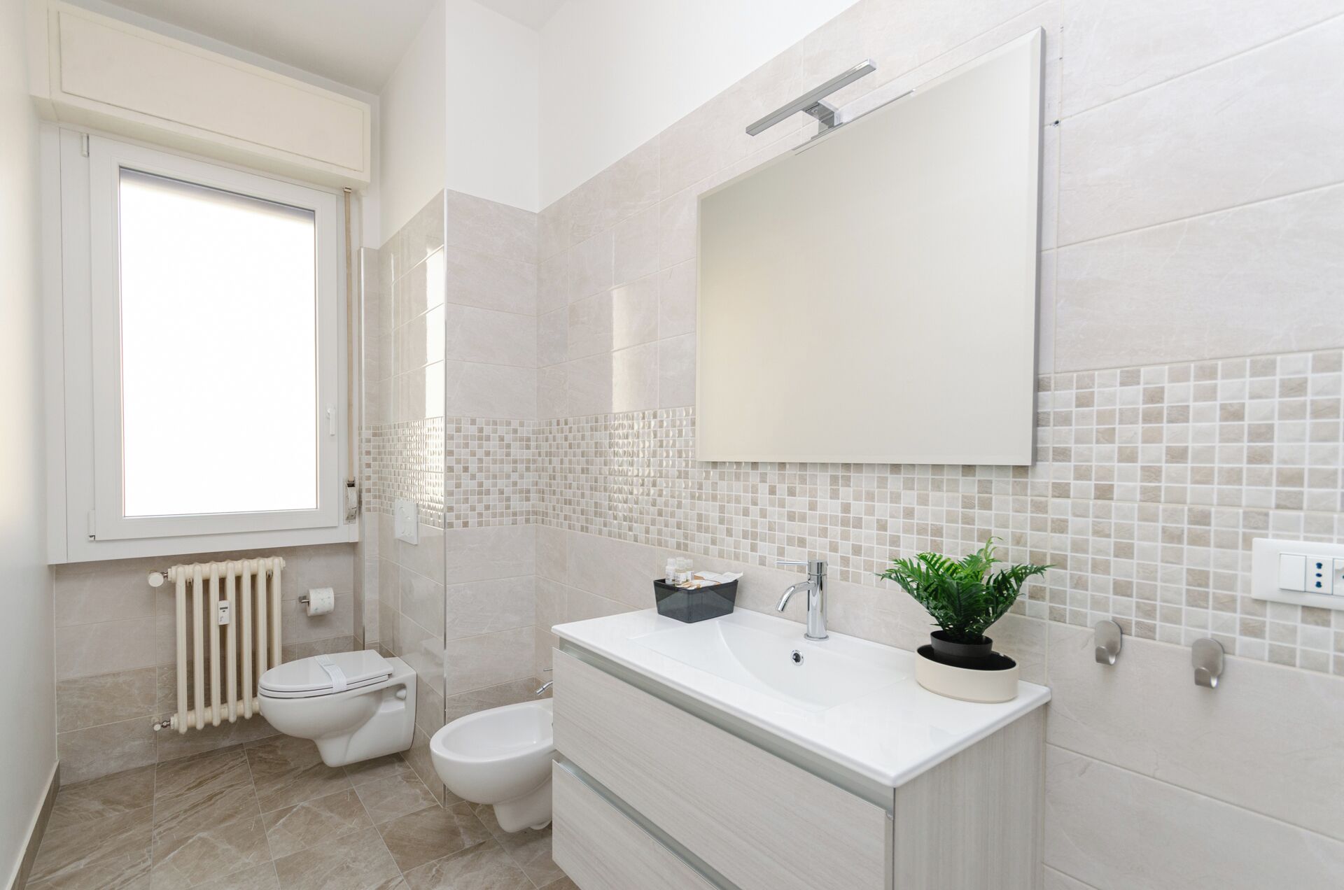 Un baño con inodoro, bidé, tocador con lavabo y espejo, y un radiador.