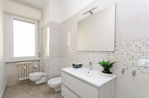 A bathroom with a toilet, bidet, vanity with a sink and mirror, and a radiator.