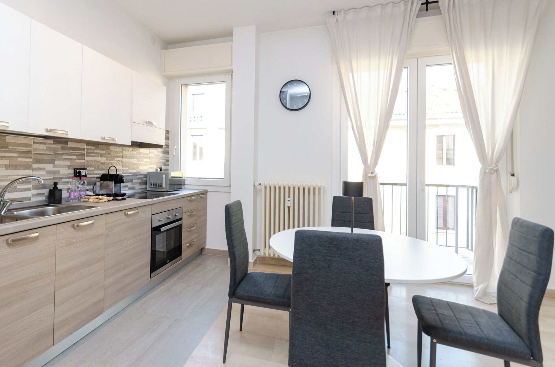 A modern kitchen with a built-in oven, microwave, and kettle. There is a dining area with a round table and four chairs.
