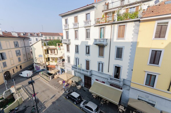 A multi-story building with balconies, a café on the ground floor, and a parking area.