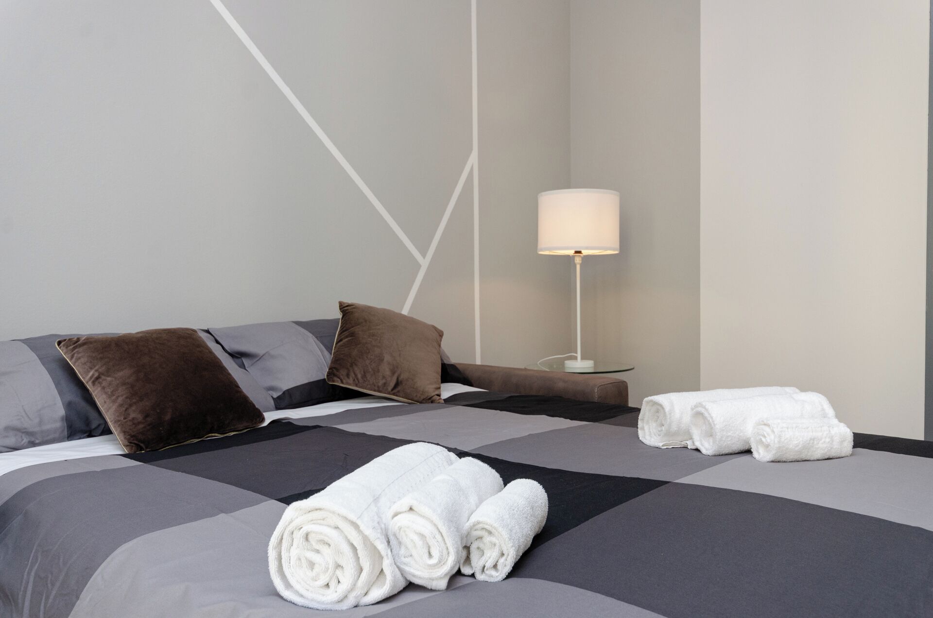 A hotel room with a bed, pillows, a lamp, and towels.
