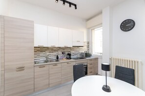A modern kitchen with light wood cabinets, a tiled backsplash, a built-in oven, and a dining area with a table and chairs.