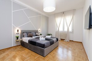 Een moderne slaapkamer met een groot bed, een nachtkastje met lamp, een potplant en een raam met gordijnen.