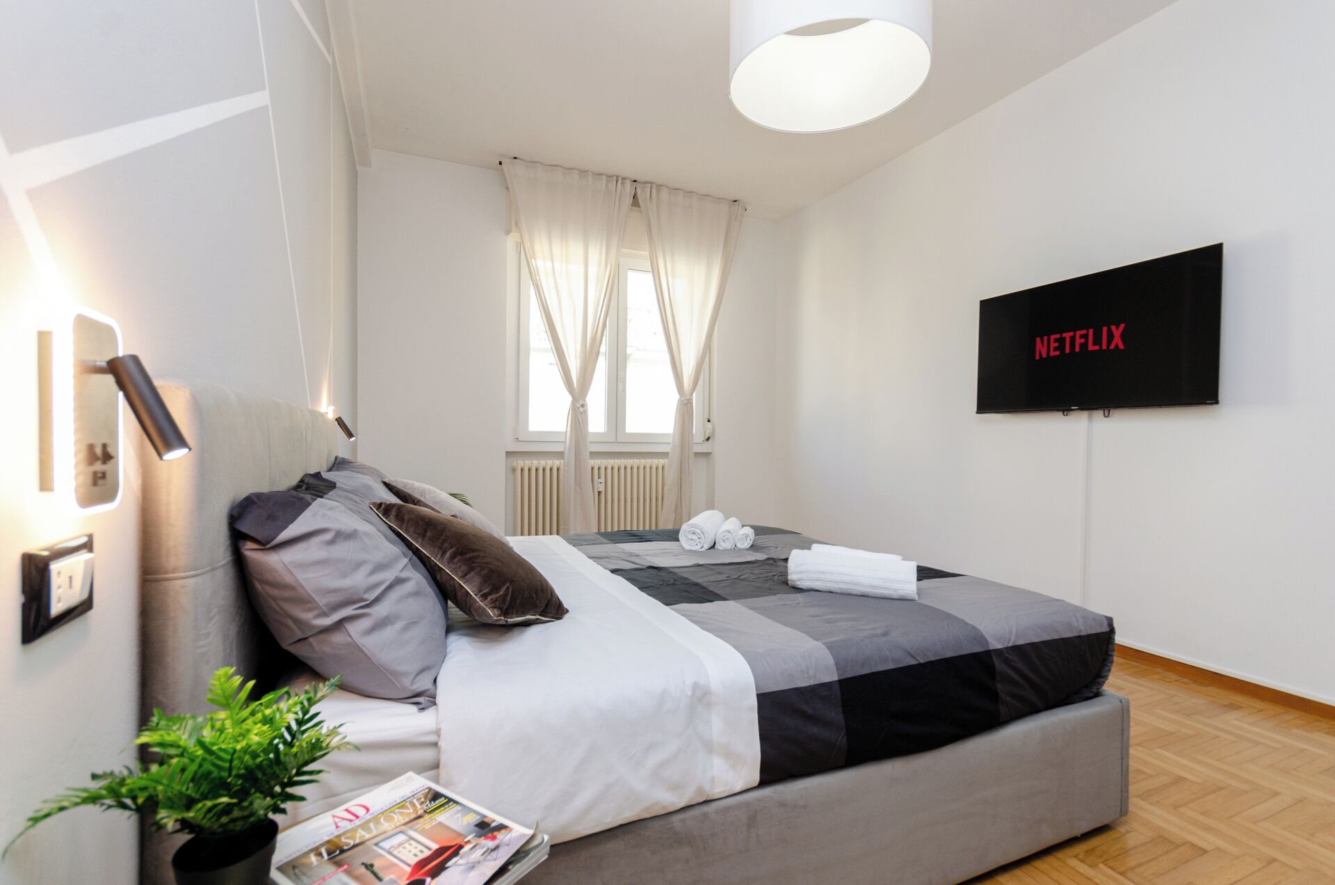 A modern bedroom with a bed, a TV, and a magazine on the nightstand.