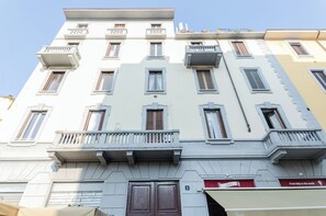 A multi-story building with balconies, a ground-level entrance, and a sign indicating a restaurant.