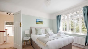 Une chambre à coucher avec un grand lit, une table de chevet, une commode, une fenêtre avec des rideaux et une porte donnant sur une autre pièce.