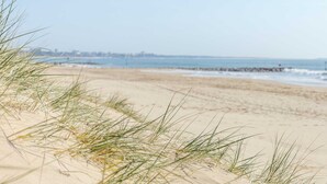 Une plage de sable avec des dunes et une vue lointaine sur une jetée.