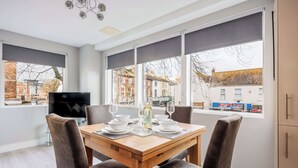 A dining area with a wooden table, four chairs, a TV, and a window with blinds. - Seafarers -  Near Poole Quay with Free Parking (Poole)