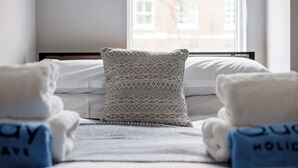 A hotel room with a bed, a patterned pillow, and towels with text. - Seafarers -  Near Poole Quay with Free Parking (Poole)
