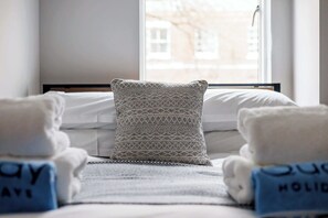 Une chambre d’hôtel avec un lit, un oreiller à motifs et des serviettes avec du texte imprimé.