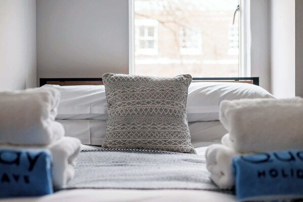 A hotel room with a bed, a patterned pillow, and towels with text.