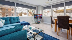 A modern living room with a blue sofa, a glass coffee table, a TV, and a dining area with a wooden table and chairs. - Seafarers -  Near Poole Quay with Free Parking (Poole)