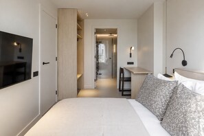 A hotel room with a bed, a desk, a television, and a bathroom visible through an open door. - Sweett | Diagonal Sagrada 6 (Barcelona)