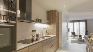 A modern kitchen with a built-in oven, a sink, and wooden cabinetry. There is a dining area with a table and chairs visible in the background.