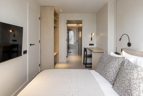 Una habitación de hotel moderna con una cama grande, un escritorio, un televisor y un vestidor.