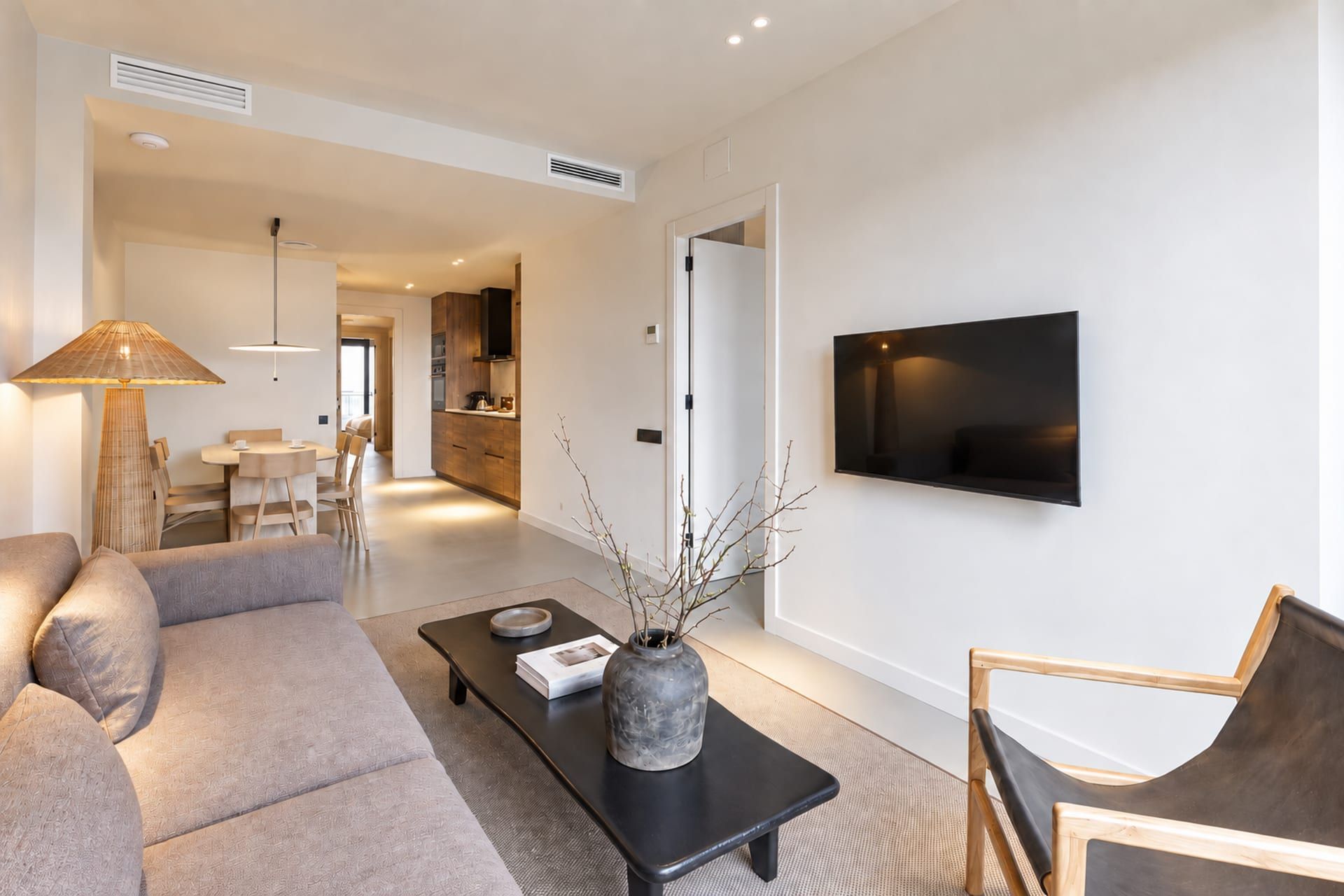 A modern living room with a sofa, a coffee table, a TV, and a dining area in the background.