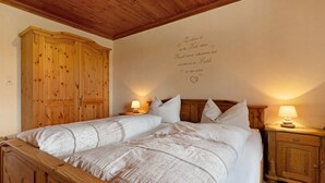 A double bed with a quilt, wooden wardrobe, bedside lamps, and a wall with a heart-shaped inscription. - Apartment 'Schwarzwaldliebe' with Mountain View, Private Terrace and Wi-Fi (Oberharmersbach)