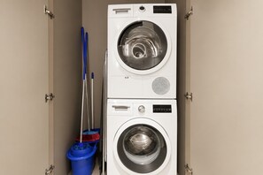 A front-loading washing machine with a control panel and a blue mop bucket.
