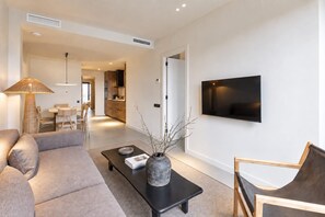 Una sala moderna con un sofá, una mesa de centro, un televisor y un área de comedor al fondo.