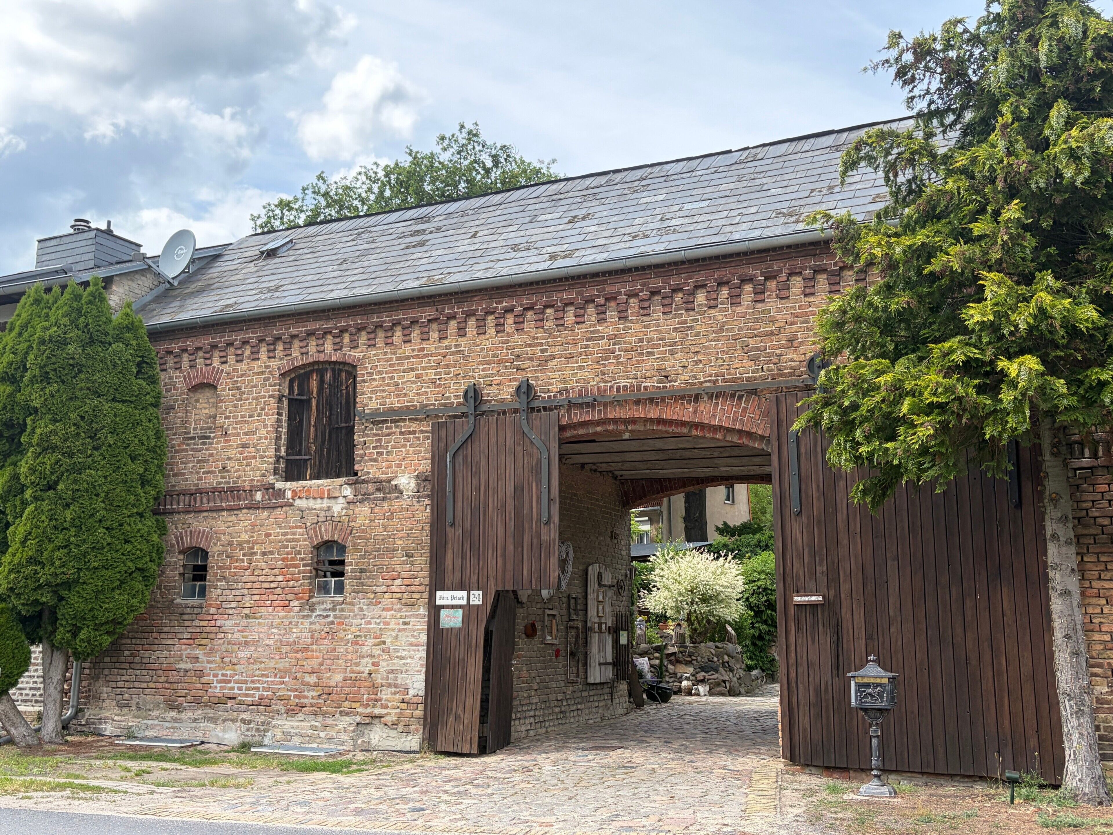 A brick building with a large wooden gate, a cobblestone entrance, and a sign indicating 'Hof Blechert.'