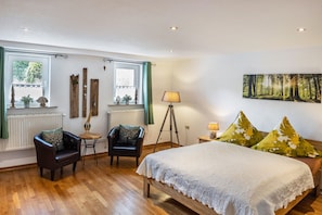 A bedroom with a bed, two chairs, a lamp, a window with curtains, a radiator, and a forest-themed painting. - Apartment 'An Der Wublitz' with Shared Terrace, Shared Garden and Wi-Fi (Werder (Havel))