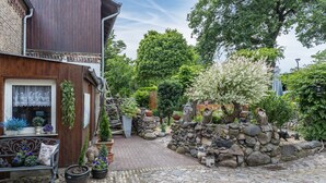 A cobblestone courtyard with a wooden building, stone wall, and various potted plants. - Apartment 'An Der Wublitz' with Shared Terrace, Shared Garden and Wi-Fi (Werder (Havel))