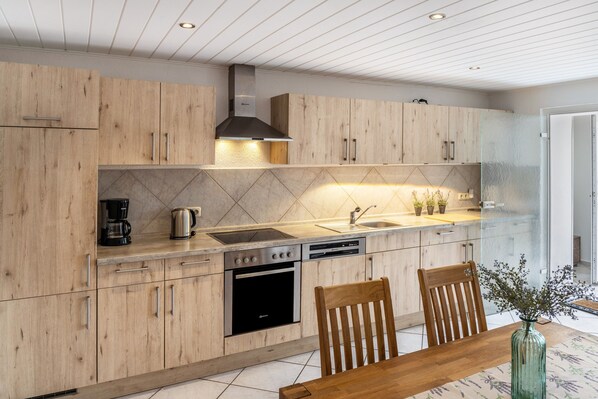 A modern kitchen with wooden cabinets, stainless steel appliances, and a dining area with a wooden table and chairs. - Apartment 'An Der Wublitz' with Shared Terrace, Shared Garden and Wi-Fi (Werder (Havel))