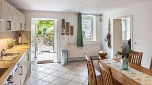 A modern kitchen with a dining area, wooden cabinets, a window with a view, and a green curtain. - Apartment 'An Der Wublitz' with Shared Terrace, Shared Garden and Wi-Fi (Werder (Havel))