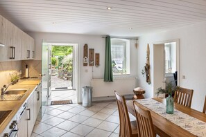 A modern kitchen with a dining area, wooden cabinets, a window with a view, and a green curtain.