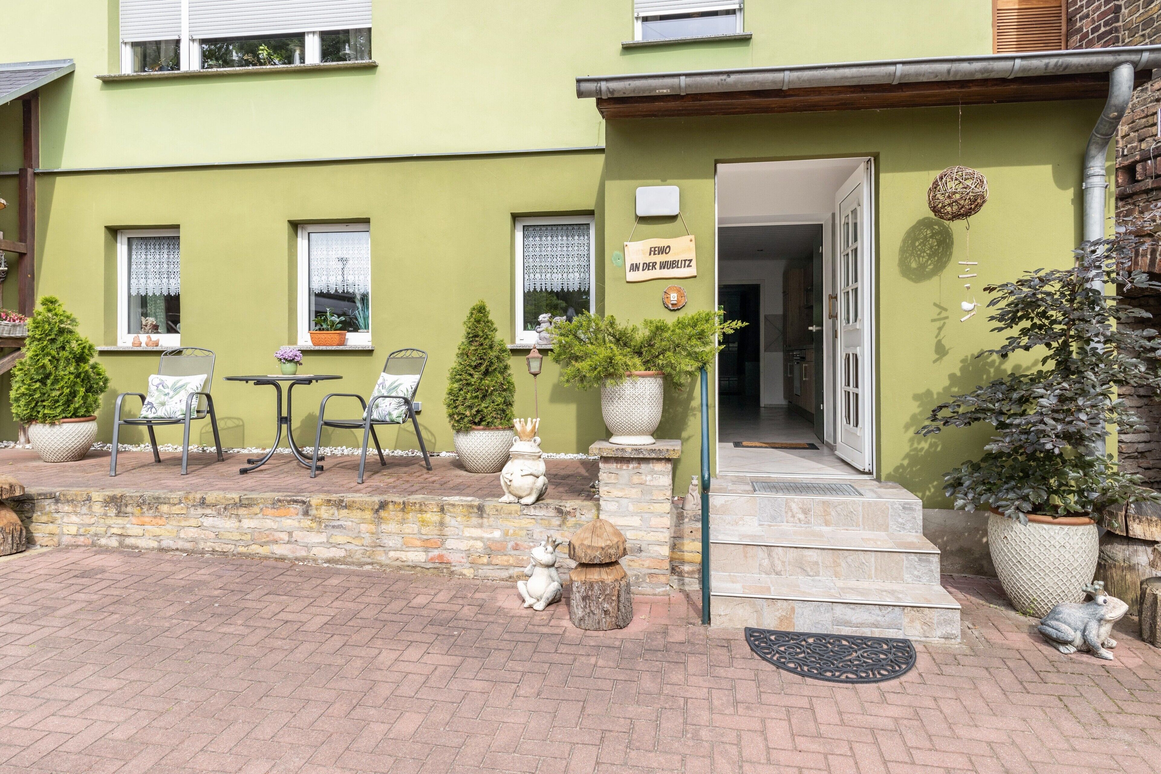 Un bâtiment à la façade verdoyante, doté d’une terrasse, de plantes en pot et d’une enseigne indiquant « FEWNO AN DER WURTZ ».