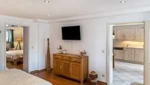 A bedroom with a bed, a wooden dresser, a flat-screen TV, and a kitchen visible through an open door. - Apartment 'An Der Wublitz' with Shared Terrace, Shared Garden and Wi-Fi (Werder (Havel))