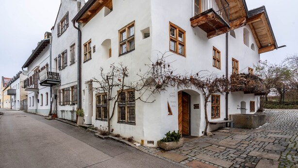 Ein traditionelles europäisches Gebäude mit Kopfsteinpflasterstraße, hölzernen Balkonen und einer Steineinfahrt.