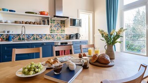 Une cuisine avec une table à manger dressée pour le petit-déjeuner, avec du pain, des œufs et des fruits.
