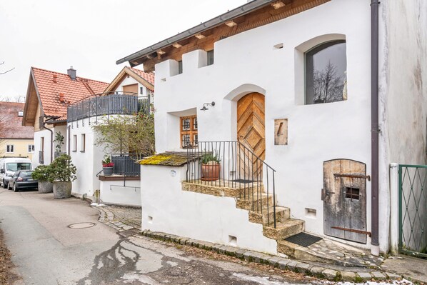 A white building with a wooden door, a balcony, and a staircase leading to the entrance.