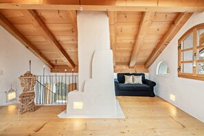 Una stanza con soffitto alto e travi in legno, un divano nero e un camino bianco.
