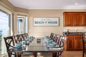 Comedor con una mesa larga dispuesta para seis comensales, armarios de madera y una zona de cocina con mostrador.