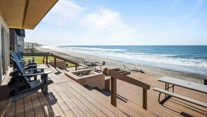 A wooden deck with lounge chairs and picnic tables overlooking a beach.
