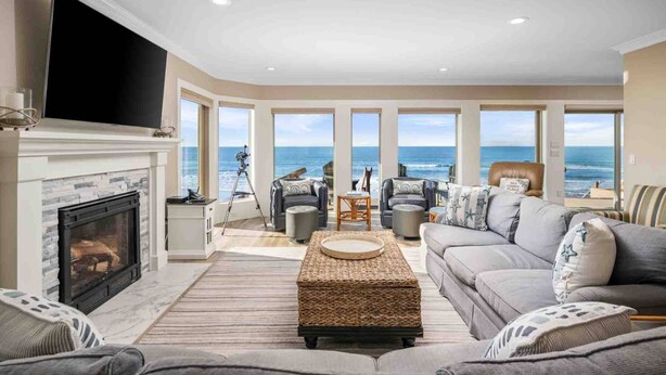 A spacious living room with a fireplace, large windows offering ocean views, and comfortable seating.