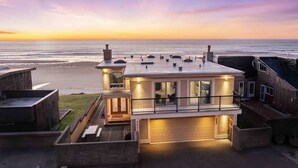 A coastal building with a balcony overlooking the beach, a garage, and a small garden area.