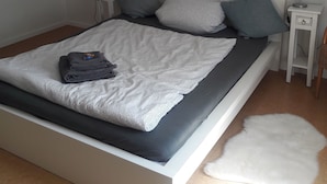 Ein modernes Schlafzimmer mit einem großen Bett, zwei Nachttischen, einer Wandlampe und einem flauschigen weißen Teppich.