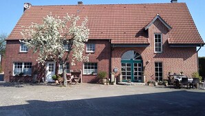 Ein zweistöckiges Backsteingebäude mit rotem Ziegeldach, einer grünen Tür und einer kleinen Veranda mit Sitzgelegenheiten.