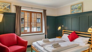 A room with a bed, a red chair, a window with curtains, and two wall-mounted lamps.