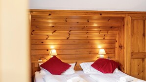Une pièce aux murs lambrissés, comprenant deux lits, chacun avec du linge de lit blanc et des oreillers rouges, ainsi que des lampes de chevet.