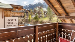 Un balcon en bois offrant une vue sur les montagnes, une enseigne indiquant le restaurant de l’hôtel Diana, et une chaise en métal.