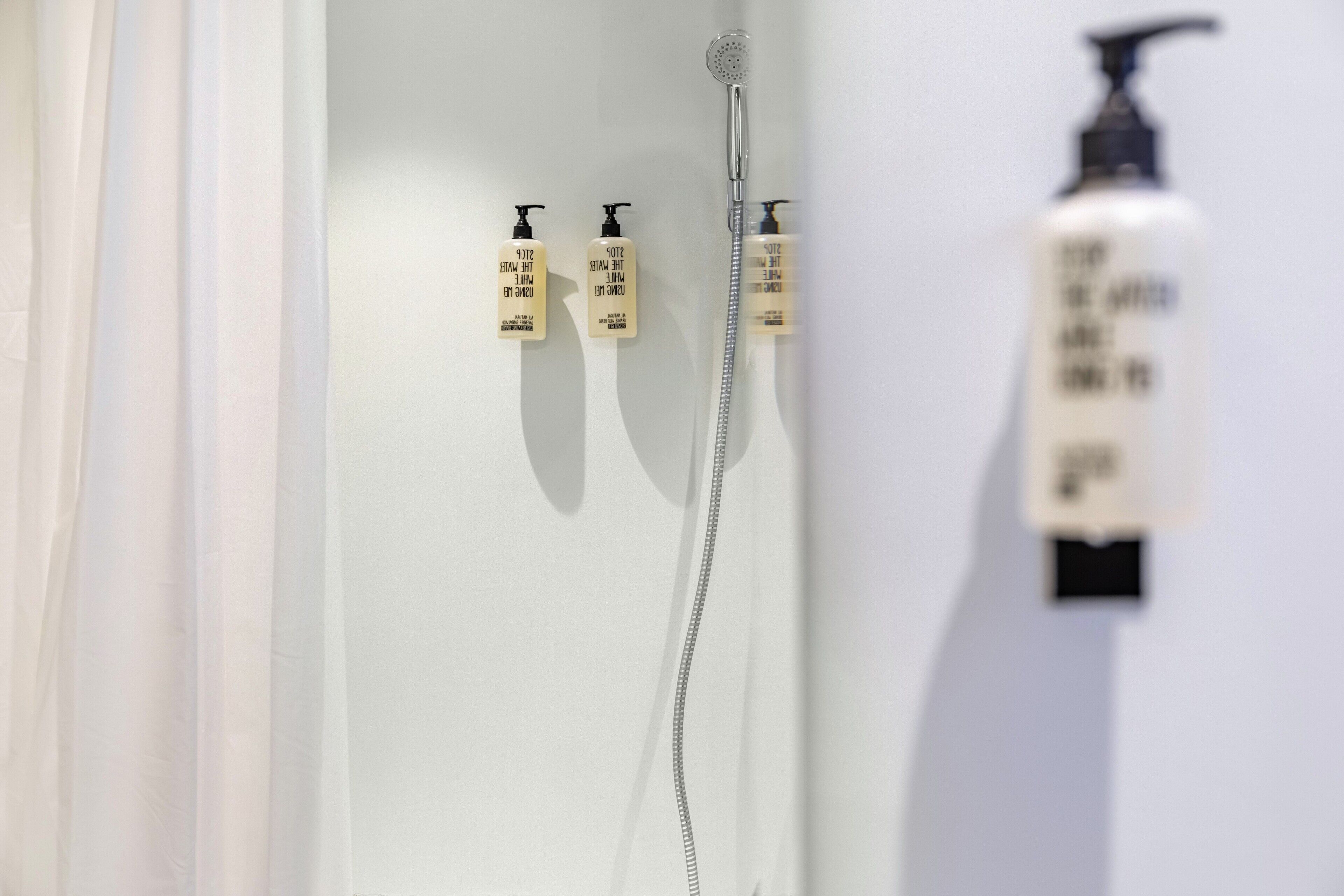 Une salle de bain avec une douche, deux bouteilles de shampoing et un flacon de lotion accroché au mur.