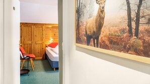 Una habitación con una cama, una silla, un armario de madera y un cuadro de un ciervo en la pared.