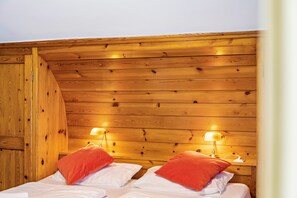 Ett rum med träpanel på väggarna, med två sängar, var och en med en röd kudde och en sänglampa.