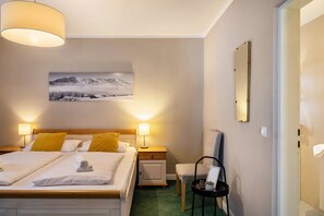 A hotel room with two beds, a nightstand with a lamp, a chair, a small table with a remote, and a framed picture on the wall. - Room 8 (budget double room) with mountain view, balcony and Wi-Fi (Seefeld in Tirol)