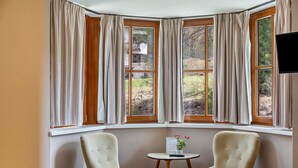 A room with a corner window, two armchairs, a small table with a menu and a plant, and a TV on the wall. - Room 5 Deluxe family room 2+1 (extra bed available for children) with mountain view, balcony (Seefeld in Tirol)