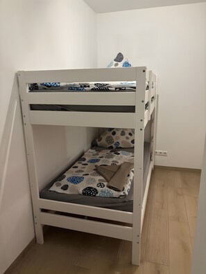 Una cama litera con ropa de cama estampada, un cajón y un estante en la pared.